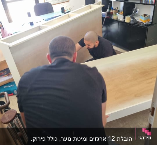 שני אנשים מרימים רהיט במשרד עם מדפים וספרים